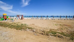 Una playa con área de juegos para niños, sombrillas y sillas reclinables.