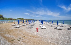 A beach with rows of sun loungers and blue umbrellas, a red cooler, and a clear sky. - Awesome home in Torino di Sangro with WiFi (Torino di Sangro)