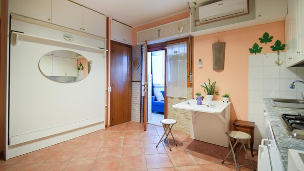 A kitchen with white cabinets, a round mirror, a small dining table with chairs, and a blue sofa in the adjacent living area. - Awesome apartment in Martinsicuro with WiFi (Martinsicuro)