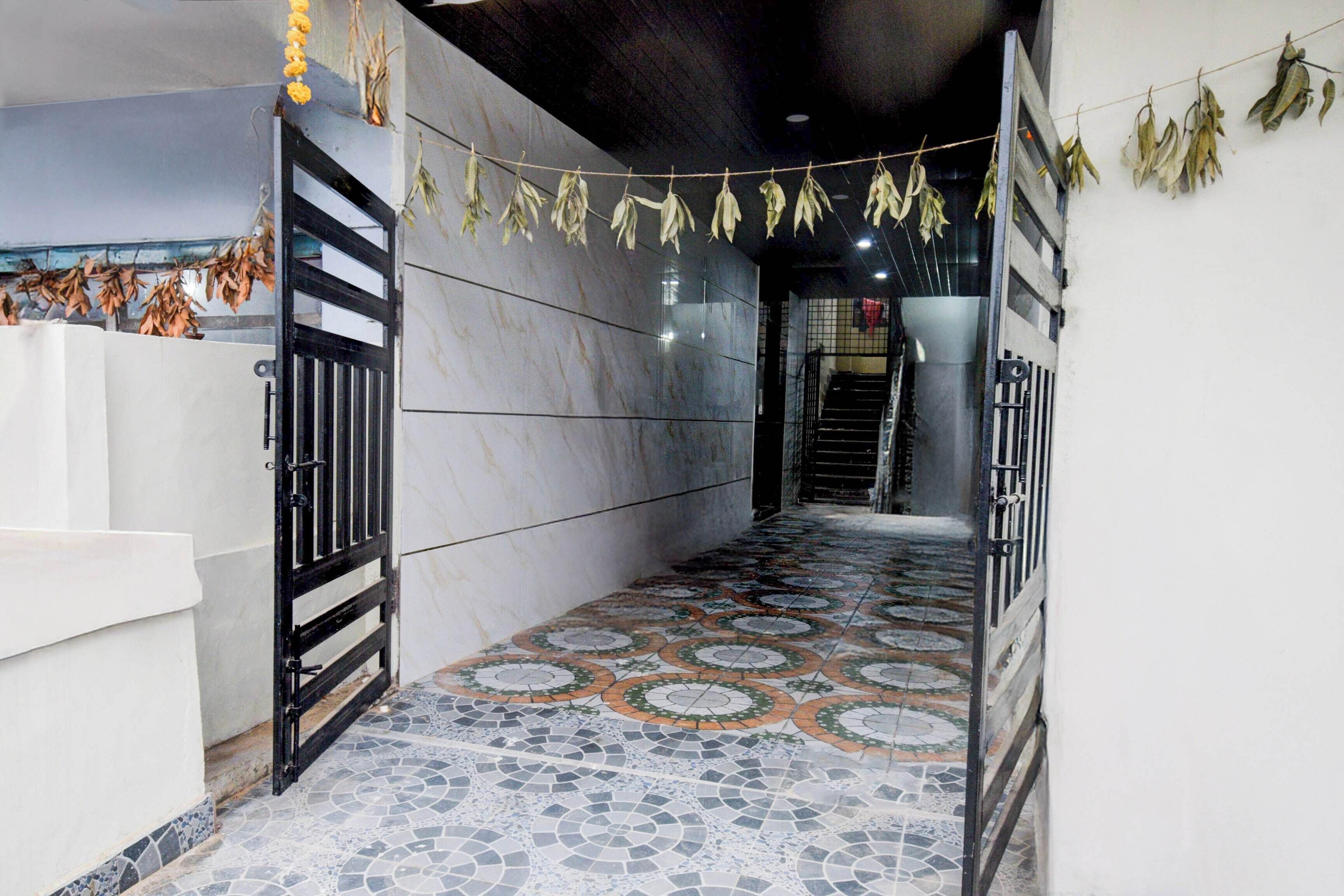 Un pasillo con suelo de baldosas estampadas, una reja de metal negro y una pared decorada con hojas secas colgantes.