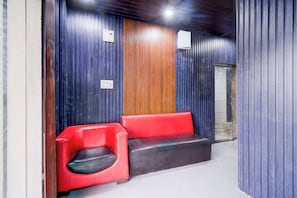 A reception area with a red and black bench, wooden panel wall, and a door leading to another room. - Collection O Srisailam Highway (Hyderabad)