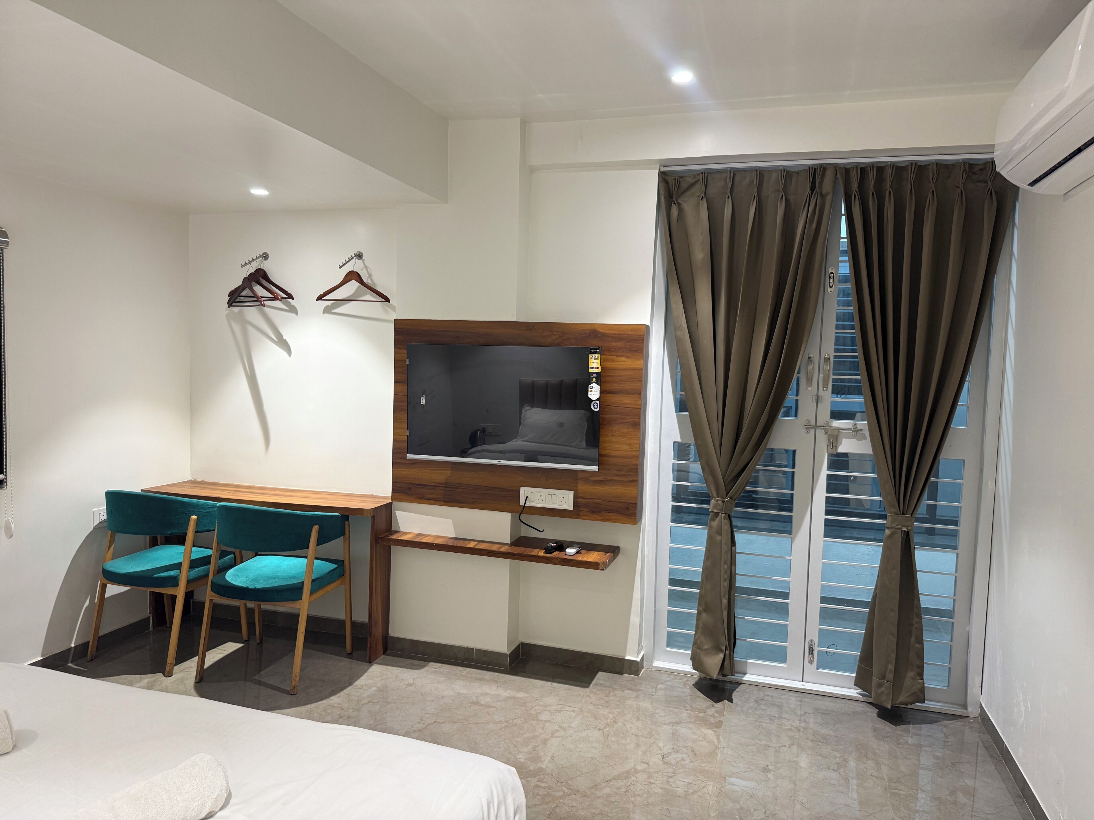 Habitación de hotel con una cama, un escritorio con silla, un televisor montado en la pared y una ventana con cortinas.