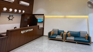 A reception area with a wooden desk labeled 'RECEPTION,' a chandelier, air conditioning units, and a sofa. - Hotel Skyboat Inn (Nashik)
