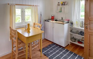 A compact kitchen with a wooden table, chairs, a refrigerator, and a window with curtains. - Cozy home in Averøy with WiFi (Averøy)