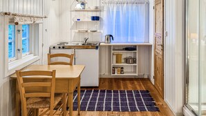 A compact kitchen with a dining table, chairs, a stove, and a small window with curtains. - Cozy home in Averøy with WiFi (Averøy)