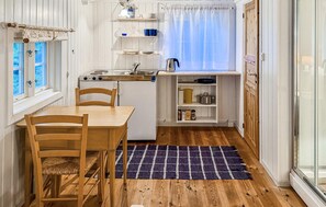 Eine kleine Küche mit Esstisch, Stühlen, einem Herd und einem kleinen Fenster mit Vorhängen.