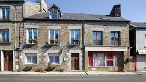 Una hilera de edificios de piedra con numerosas ventanas, algunas con jardineras, y una fachada visible con un toldo rojo.