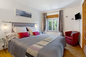 Un dormitorio con cama, una silla roja, televisión y ventana con cortinas.