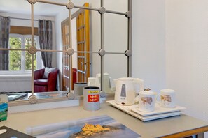 Una habitación de hotel con ventana, una mesa con hervidor, tazas y un pequeño cuadro.