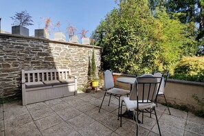 Un patio con muros de piedra, un banco de madera y mobiliario exterior.