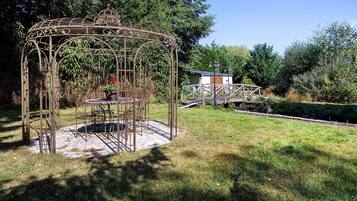 A gazebo with a circular base and intricate metalwork, surrounded by a grassy area and trees.