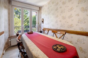 A dining area with a table set for two, a window with a view of trees, and a radiator on the wall. - Bed and Breakfast 'La Prairie De Vassy 14 - Chausey' with Shared Terrace, Wi-Fi and Air Conditioning (Valdallière)