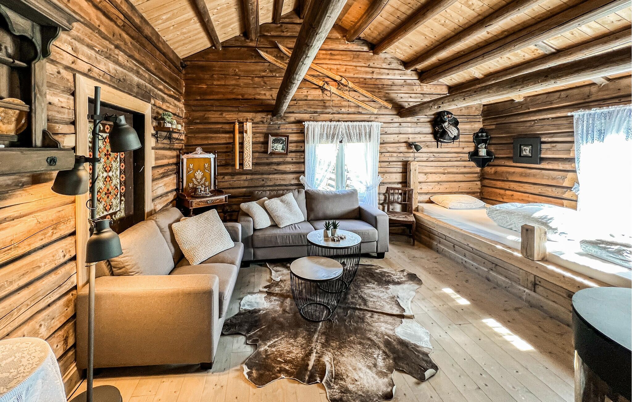 Interior de una cabaña de madera con un sofá, una mesa de centro y un manto de piel.