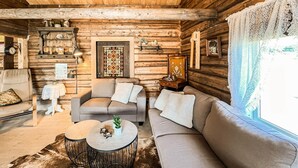 Interior acogedor de una cabaña de troncos con sofá, sillón y mesa de centro redonda.