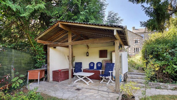 A covered outdoor seating area with a table and chairs, a wooden bench, and a potted plant.