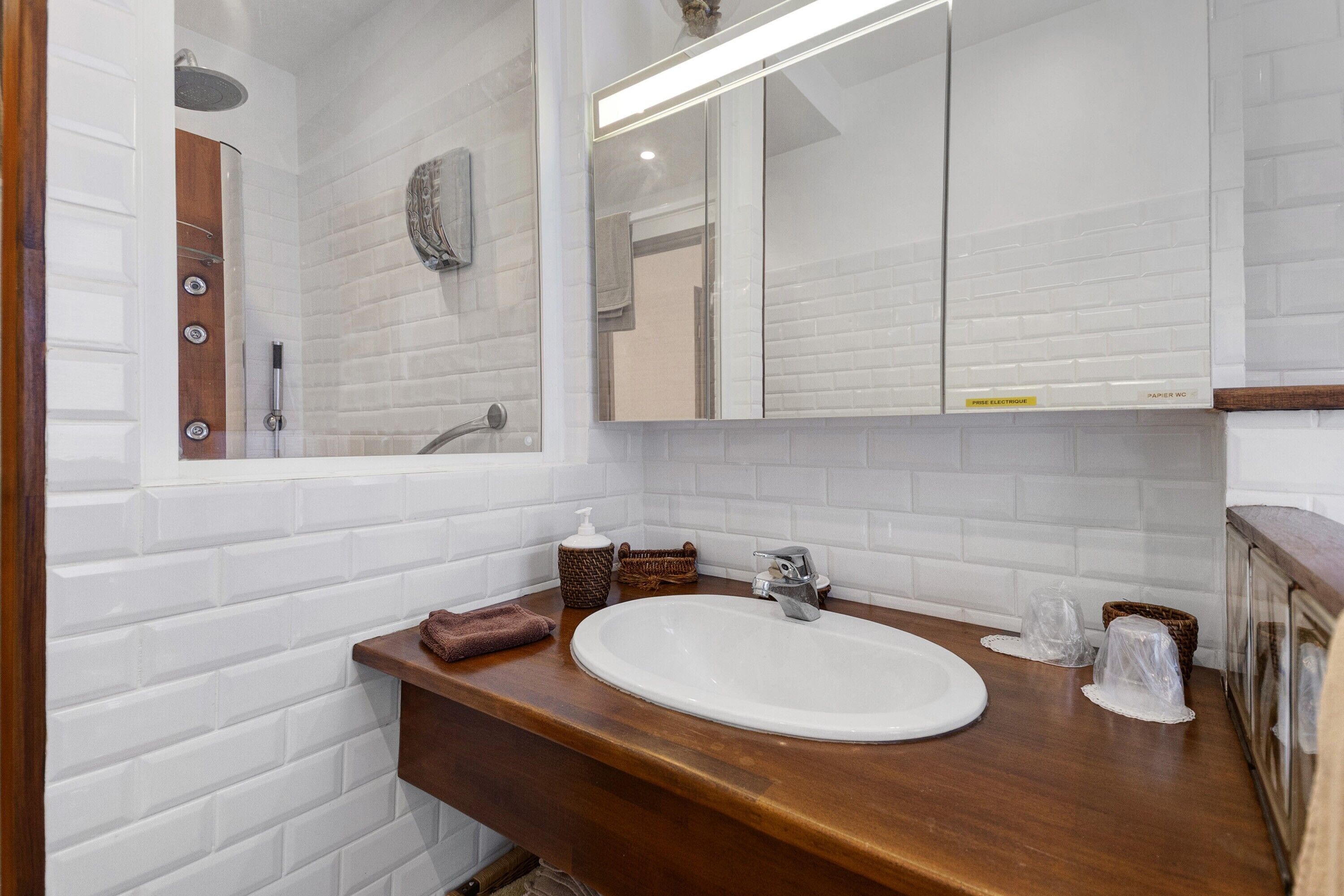 Un bagno con un lavandino bianco, un piano d'appoggio in legno e uno specchio sopra.