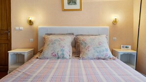 A bedroom with a striped bedspread, floral pillows, and two bedside tables with wall-mounted lamps.
