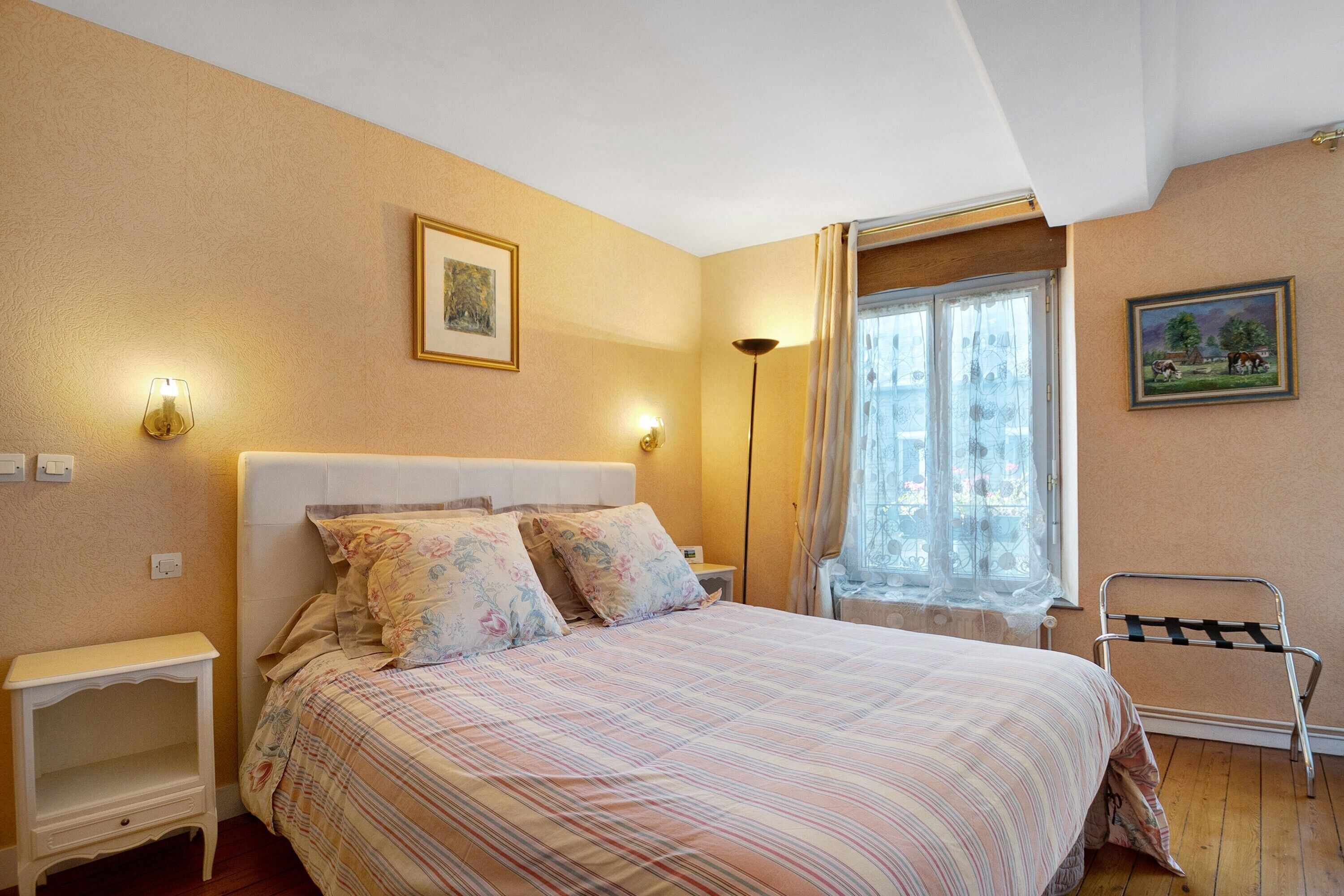 Un dormitorio con cama, mesitas de noche, una ventana con cortinas y un cuadro en la pared.