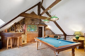 Acogedor dormitorio en el ático con mesa de billar, taburetes de madera, zona de bar y pared de piedra.