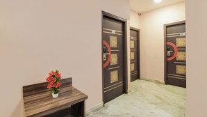 Um corredor com piso de mármore, um balcão de recepção com um vaso de flores e portas com números e desenhos decorativos.