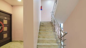Uma escadaria com corrimãos de metal, uma porta com design circular e uma câmera de segurança no teto.