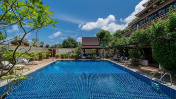 A swimming pool with a tiled deck, surrounded by potted plants and lounge chairs.