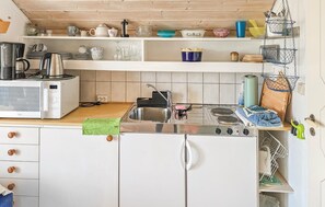 Cocina con estufa, pileta y microondas. Hay repisas sobre la mesada con diferentes vajillas y una cesta colgante con utensilios.
