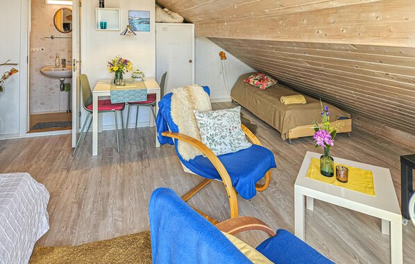 Una habitación acogedora con techo de madera, un rincón de comedor con mesa y sillas, un sofá con cojín floral y una pequeña mesa con un jarrón de flores.