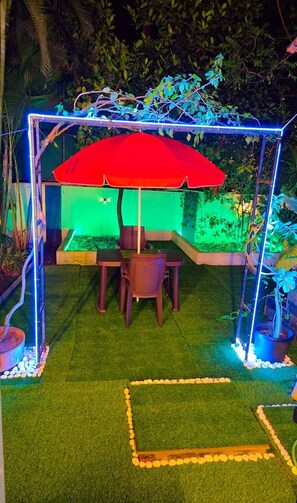 An outdoor seating area with a red umbrella, surrounded by greenery and artificial lighting. - 3 BHK NEAR CANDOLIM BEACH, NORTH GOA - THE LEAFY RETREATÉ BY G AND S PRIVEÉ (Calangute)