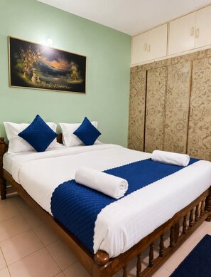 A neatly made bed with blue and white bedding, a painting on the wall, and a patterned wardrobe. - 3 BHK NEAR CANDOLIM BEACH, NORTH GOA - THE LEAFY RETREATÉ BY G AND S PRIVEÉ (Calangute)