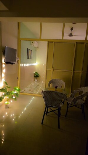 A room with a dining table and chairs, a potted plant, and a wall-mounted television. - 3 BHK NEAR CANDOLIM BEACH, NORTH GOA - THE LEAFY RETREATÉ BY G AND S PRIVEÉ (Calangute)