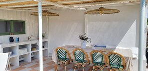 A covered outdoor dining area with a table and chairs, a shelf with kitchen items, and a hanging light fixture. - Superbe maison de 4 chambres, piscine chauffée à Gujan-Mestras (Gujan-Mestras)