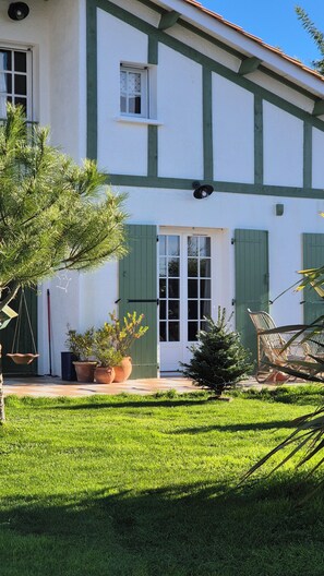 A two-story building with a green and white exterior, a front door, and a small front yard with grass and potted plants. - Superbe maison de 4 chambres, piscine chauffée à Gujan-Mestras (Gujan-Mestras)