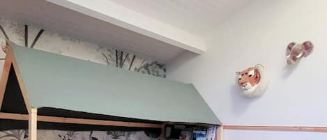 A child's bunk bed with a green canopy, a wall-mounted animal head, and a small toy train set.