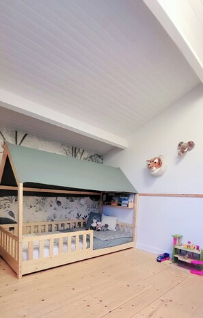 Ein Kinderstockbett mit einem grünen Baldachin, einem an der Wand befestigten Tierkopf und einem kleinen Spielzeug-Zugset.