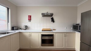 A kitchen with white cabinets, a stainless steel oven, a microwave, and a toaster. - Your Beach Escape Starts Here (Wannanup)