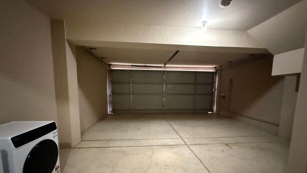 A garage with a closed garage door, a washing machine, and a light fixture on the ceiling. - Your Beach Escape Starts Here (Wannanup)