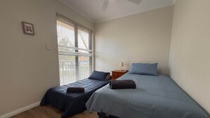 A bedroom with two single beds, a nightstand, a ceiling fan, and a window with blinds. - Your Beach Escape Starts Here (Wannanup)
