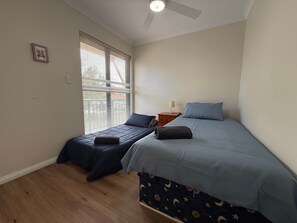 Ein Schlafzimmer mit zwei Einzelbetten, einem Nachttisch, einem Deckenventilator und einem Fenster mit Jalousien.