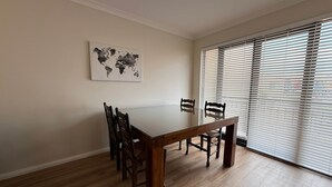 A dining area with a wooden table and chairs, a world map artwork on the wall, and a large window with blinds. - Your Beach Escape Starts Here (Wannanup)