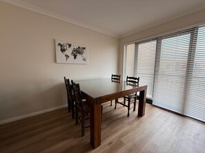 Ein Essbereich mit einem Holztisch und Stühlen, einer Weltkarte als Wandbild und einem großen Fenster mit Jalousien.