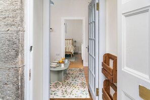 A hallway leading to a dining area with a table set for two, a bed with a striped bedspread, and a floral rug on the floor. - Cosy 1BR by Calton Hill & Royal Mile (Edinburgh)