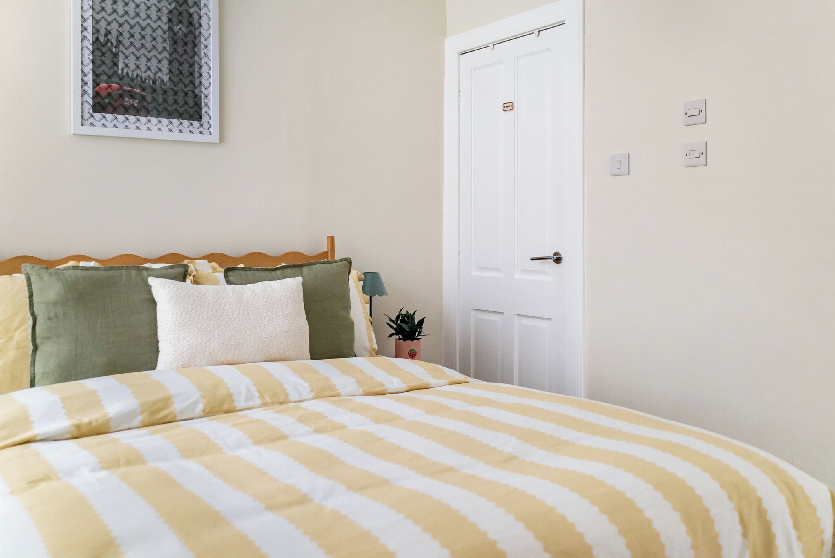 A bedroom with a bed, pillows, a nightstand, a door, and a wall-mounted item.
