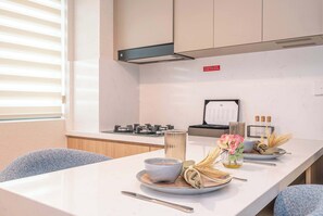 A modern kitchen with a dining table set for two, equipped with a gas stove, a kettle, and a menu board. - Longevity Superior Escape Tranquil Wellness (Jumeirah Village Triangle)