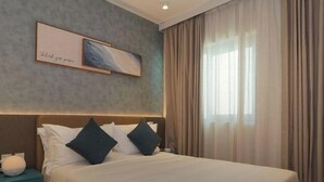 Ein Hotelzimmer mit einem Bett, einem Nachttisch, einem Wandbild und einem Fenster mit Vorhängen.