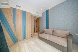 A modern living room with a sofa, a built-in washing machine, and a sliding door closet. - Longevity Superior Escape Tranquil Wellness (Jumeirah Village Triangle)