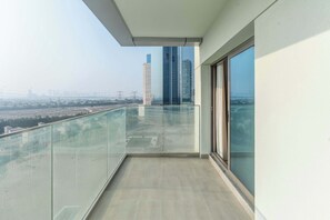 Un balcon doté d’une balustrade en verre, une vue sur le paysage urbain et un grand immeuble visible au loin.