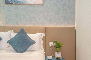 Quarto com cama, almofadas, mesa de cabeceira com planta e tomada na parede.