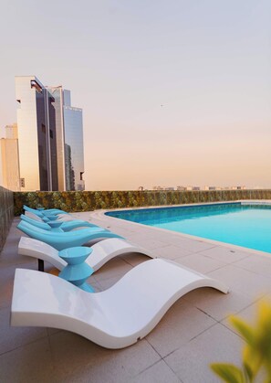 A swimming pool with lounge chairs and a modern building in the background. - Longevity Superior Escape Tranquil Wellness (Jumeirah Village Triangle)