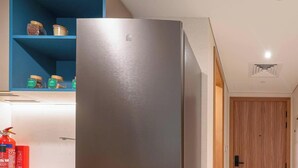 A hallway with a stainless steel refrigerator, a blue shelf with jars, a wooden door, and a fire extinguisher. - Deluxe Escape  Luxury Wellness Hotel (Jumeirah Village Triangle)